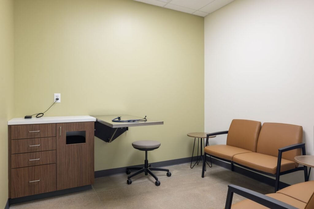 A brightly lit, modern veterinary exam room with stainless steel tables, medical supplies on shelves…